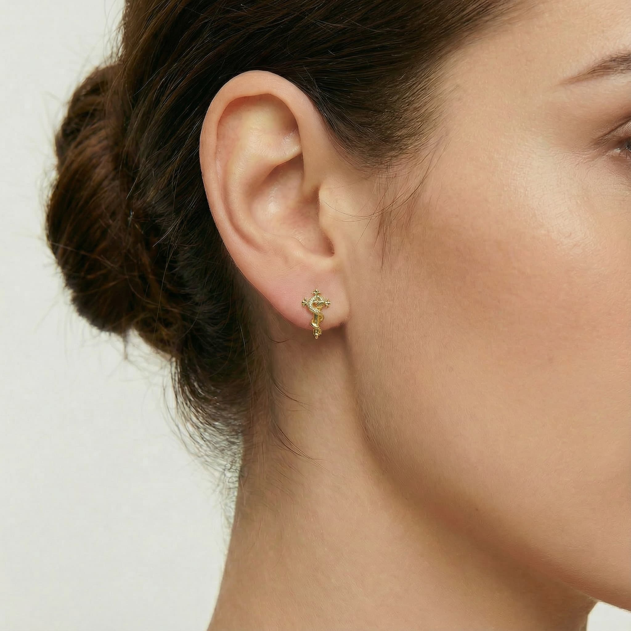 [Brand] 24K Gold Vermeil Snake Cross Stud on model, close-up earlobe jewelry shot.