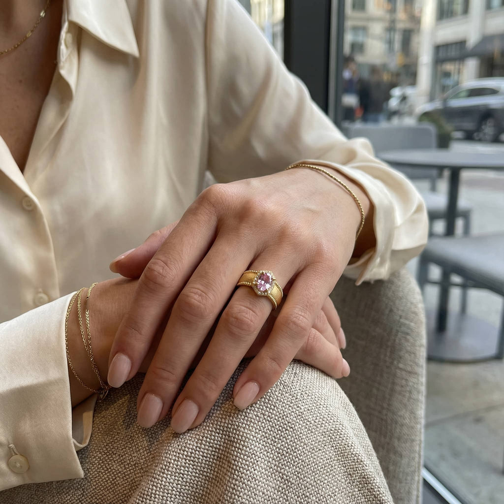 Close up of woman's hands featuring a statement gold ring with pink crystal and gold bracelets