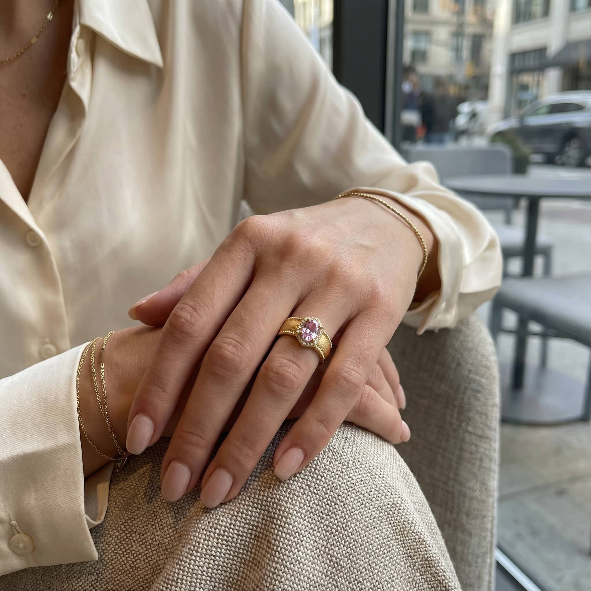 Close up of woman's hands featuring a statement gold ring with pink crystal and gold bracelets