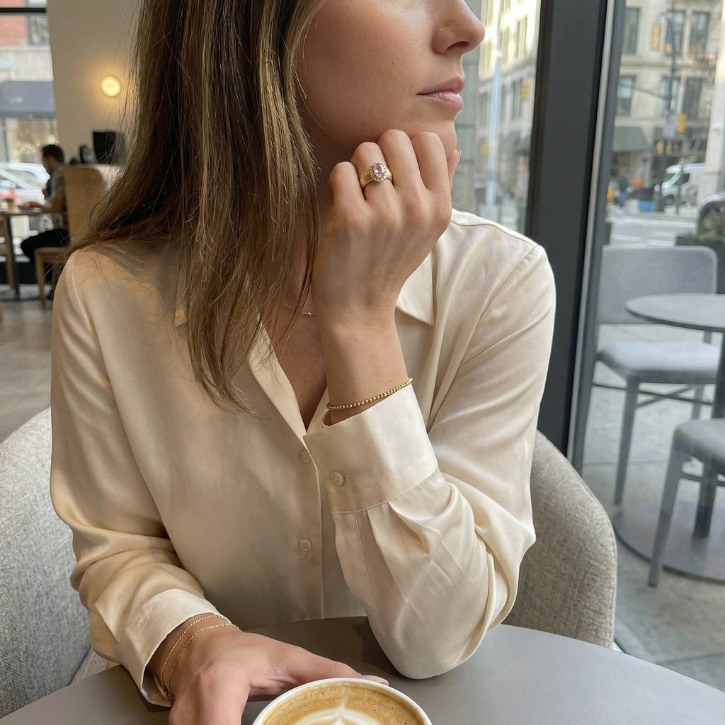 Elegant woman wearing a gold pink stone ring sitting in a cafe with a silk blouse
