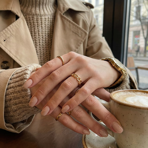 21K Gold Chain Ring displayed on a woman's hand with other gold rings, sitting beside a cup of coffee.